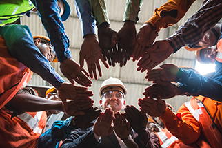 Owner looking down towards the camera in the center, with all his factory employees huddled up in a circle with their arms in the center.